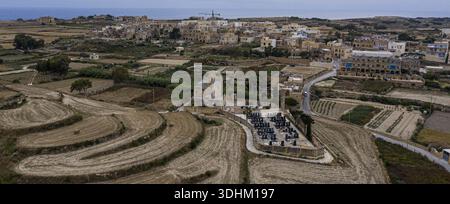 Die verwitterte Steinkirche und der düstere Friedhof stehen in krassem Kontrast zu den goldenen Feldern in Victoria, Malta. Stockfoto
