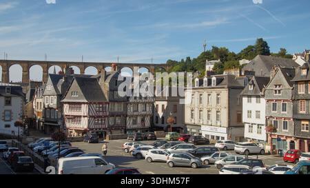 Historische Fachwerkhäuser stehen in der Nähe eines Parkplatzes, eingerahmt von einem großen Steinviadukt im Hintergrund. Stockfoto