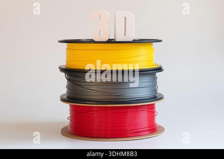 Gelbe, graue und rote Kunststofffilamente für 3D-Druck auf Spulen auf weißem Hintergrund und 3D-Text aus Kunststoff, volumetrische Kosten, Material für A Stockfoto