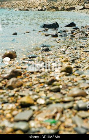 Kleine Wellen, die über Kieselsteine entlang der Küste von Pungdo Island, Südkorea, schweben und seichtes Küstenwasser, glatte Steine und eine ruhige Natur einfangen Stockfoto