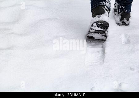Nahaufnahme der männlichen Beine in schwarzen Stiefeln, die in unberührten Schnee treten. Kopierraum, minimale Zusammensetzung Stockfoto
