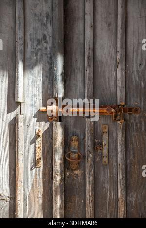 Rostiger alter Riegel und Schloss an einer dicken, rustikalen Holztür. Stockfoto