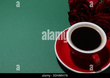 Tasse aromatischen Kaffee und rote Rosen auf grünem Hintergrund, Nahaufnahme. Leerzeichen für Text Stockfoto