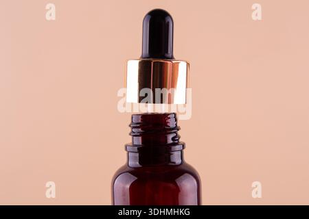 Öliger Tropfen tropft aus der Pipette in die Kosmetikflasche, isoliert auf beigefarbenem Hintergrund. Stockfoto