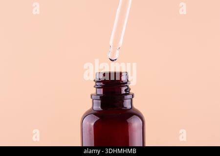 Öliger Tropfen tropft aus der Pipette in die Kosmetikflasche, isoliert auf beigefarbenem Hintergrund. Stockfoto