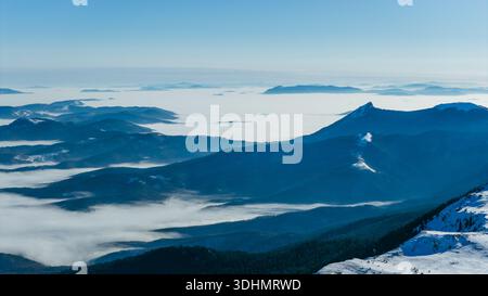 Luftpanorama des Berges Jahorina mit schneebedeckten Gipfeln, die über nebeligen Tälern ragen und die dramatische Winterlandschaft und den geschichteten Berg hervorheben Stockfoto