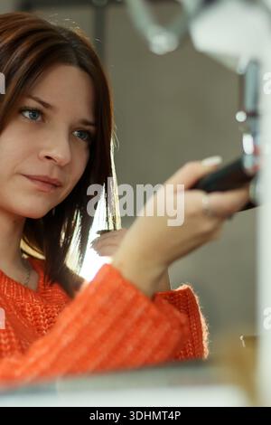 Profil der Brünette im gemütlichen Pullover, der Kaffeeausrüstungen mit introspektivem Ausdruck im Geschäft verarbeitet. Stockfoto