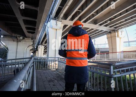 Rückansicht eines Ingenieurs in orangefarbenem Helm und Weste, der Betonbrücken im Freien vermisst. Stockfoto