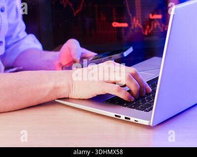 Person, die Laptop und Smartphone verwendet, um rote abnehmende Finanzdiagramme zu verfolgen Stockfoto