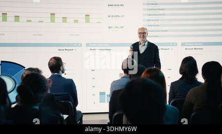 Ein breites Publikum klatscht den Geschäftsmann mit Mikrofon in die Hände, ein Mann auf der Bühne, um die internationale Konferenz mit Geschäftsleuten im Auditorium zu präsentieren. Stockfoto