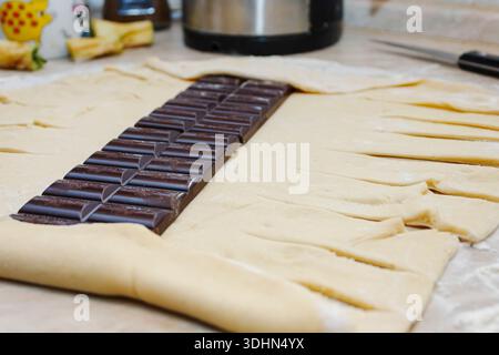 Ganze dunkle Schokoladenriegel auf rohem Teig mit geschnittenen Streifen zum Flechten. Schokoladengebäck-Dessert. Stockfoto