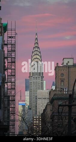 New York, NY - 20. Dezember 2025: Gebäude in Manhattan mit Skyline des Chrysler Building in der Abenddämmerung mit rosa Sonnenuntergang. Vertikale Ausrichtung. Stockfoto