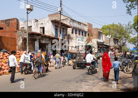 Fatehpur Sikri, Indien - 12. März 2024: Das Bild zeigt eine belebte Straße, in der Menschen laufen, Motorräder, Fahrräder, ein Traktor und Marktstände, die Tontöpfe verkaufen, vor alten Gebäuden in Fatehpur Sikri. Stockfoto
