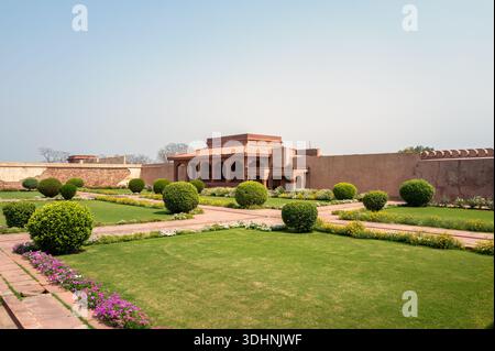 Fatehpur Sikri, Indien - 12. März 2024: Das Bild zeigt den roten Sandstein Diwan-E-AAM-Publikumssaal des Jodha Bai Palastkomplexes mit gepflegten Rasenflächen, Blumenbeeten und getrimmten Büschen im Vordergrund unter klarem Himmel. Stockfoto