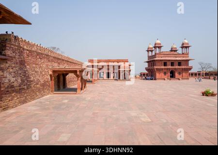Fatehpur Sikri, Indien - 12. März 2024: Das Bild zeigt die Sitzstruktur des Astrologen aus rotem Sandstein und die Diwan-i-Khas Halle mit vier Chhatris im Palastkomplex von Fatehpur Sikri, mit einem offenen Innenhof und sichtbaren Besuchergruppen. Stockfoto