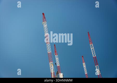 Vier Baukräne, rot und weiß, vor einem klaren blauen Himmel, horizontal Stockfoto