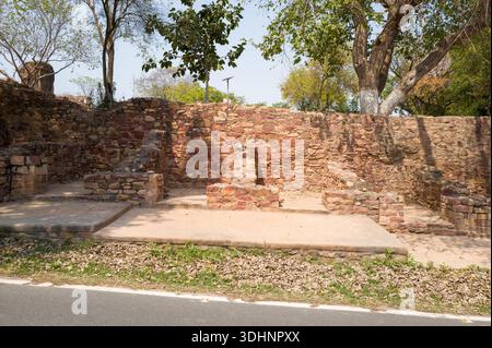 Fatehpur Sikri, Indien - 12. März 2024: Das Bild zeigt alte Steinfundamente und niedrige Mauern aus rotem und braunem Stein, teilweise von Bäumen beschattet, an einer archäologischen Ausgrabungsstätte im Freien in Fatehpur Sikri. Stockfoto