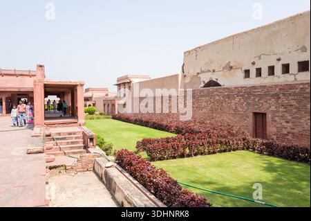 Fatehpur Sikri, Indien - 12. März 2024: Das Bild zeigt Besucher, die in der Nähe der roten Sandsteinstrukturen und gepflegten Hofgärten des Jodha Bai Palace Complex in Fatehpur Sikri unter klarem Himmel spazieren. Stockfoto