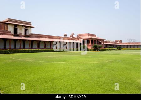 Fatehpur Sikri, Indien - 12. März 2024: Das Bild zeigt einen großen gepflegten Rasen, der von roten Sandsteinkolonnaden und Pavillons im Jodha Bai Palace Complex in Fatehpur Sikri unter klarem Himmel umgeben ist. Stockfoto