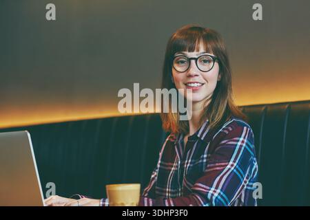Porträt, Freiberufler und Laptop mit Frau im Café für Kommunikation, Blog-Newsletter und Recherche. Online-Rezension, Verbindung und medienartikel Stockfoto