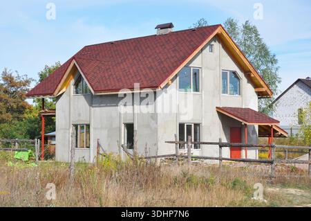 Asphaltschindeln Dachreparatur. Fassaden-Wärmedämmung und Lackierarbeiten während Renovierungsarbeiten im Außenbereich. Unvollendetes Haus mit Dachkonstruktion Stockfoto