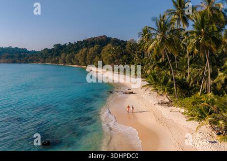 Erleben Sie die Ruhe mit einem Paar gemächlicher Hand in Hand am Takhian Beach, umgeben von üppigen Palmen und dem ruhigen türkisfarbenen Wasser von K Stockfoto