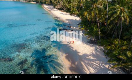 Ein Paar erlebt die Ruhe des Takhian Beach auf Koh Kood, Thailand, wo zwei Besucher entlang des weichen, pudrigen Sandes unter tropischem Wasser spazieren gehen Stockfoto