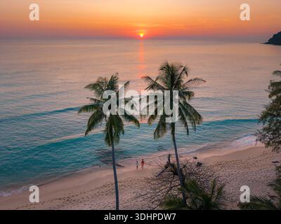 Erleben Sie die ruhige Schönheit des Takhian Beach in Koh Kood, Thailand, während sich die leuchtenden Farben des Sonnenuntergangs auf dem ruhigen Wasser spiegeln. Ein paar Männer und ein AA Stockfoto