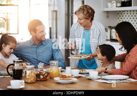 Fröhliche Familie, Pfannkuchen und Frühstück mit Oma für einen Snack am Morgen oder für eine gemeinsame Verbindung zu Hause. Mom, Dad und Großmutter, die mit Kindern essen, Kinder Stockfoto