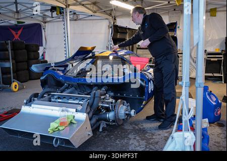 Vorderansicht eines spektakulären blauen Lola T70 Mk. 3B-Rennwagen mit ausgebauter Karosserie im Boxenbereich, während ein Mechaniker ihn auf Stühlen auflegt Stockfoto