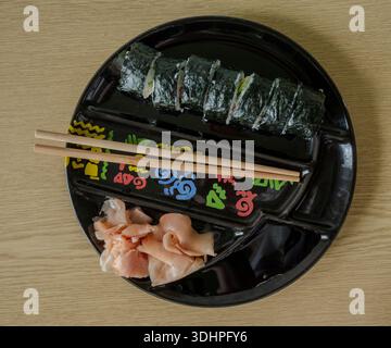 Top View of Sushi Rolls mit Essstäbchen und eingelegtem Ingwer auf schwarzer Platte, Japanese Cuisine Food Blog Foto for Kitchen and Cooking Creators Stockfoto