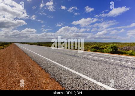 Leerer Highway durch Küstenbusch in der Nähe von Cervantes, Western Australia unter blauem Himmel mit Wolken Stockfoto
