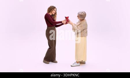 Junge Frau, die der älteren Mutter im Studio eine Geschenkbox schenkt. Stockfoto