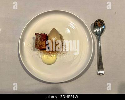 Ein kunstvoll präsentiertes Dessert besteht aus einem Stück reichhaltigen Kuchen, einem hellbraunen Eis und einem runden Pudding auf einem weißen Teller. Stockfoto