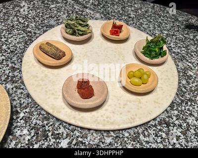 Sechs verschiedene kleine Vorspeisen in verschiedenen Farben und Texturen werden kunstvoll in einzelnen Schüsseln auf einem runden Teller präsentiert. Stockfoto