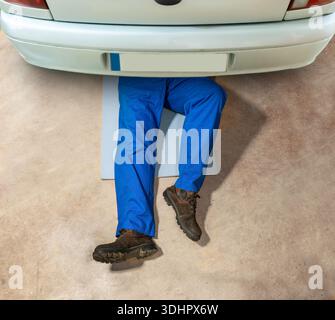 Hochwinkelaufnahme eines nicht erkennbaren Reparaturmannes, der unter seinem Auto arbeitet. Stockfoto