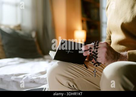 Mann mittleren Alters betet drinnen Rosenkranz und Bibel Stockfoto
