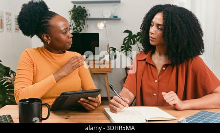 Zwei Frauen arbeiten an Einem Schreibtisch im Heimbüro mit Notebook und Tablet in Einem gemütlichen Studio zusammen Stockfoto