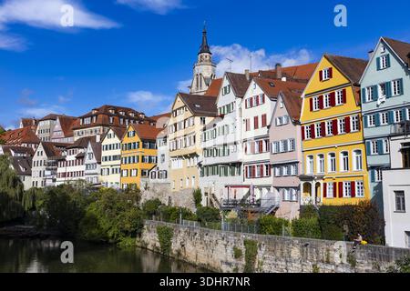 Blick auf bunte Fachwerkhäuser mit roten Fensterläden säumen ein Flussufer unter hellblauem Himmel, in der Ferne erhebt sich ein Kirchturm, Tübingen, Ba Stockfoto