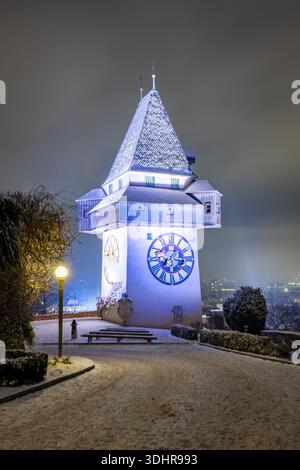 Blick auf den beleuchteten Glockenturm, der majestätisch am Nachthimmel steht, seine Details mit Schnee bedeckt und sanft über der Stadt, Graz, St. Stockfoto