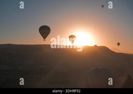 Kappadokien, Türkiye – 3. Oktober 2024: Heißluftballons schweben während einer Ballontour bei Sonnenaufgang über die felsige Landschaft Kappadokiens Stockfoto