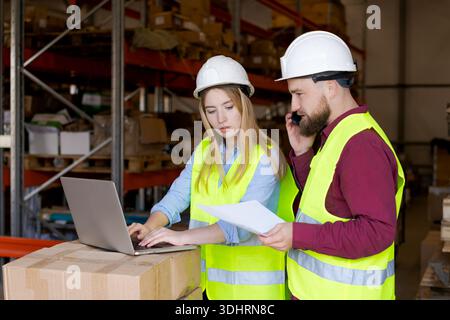 Weibliche Mitarbeiterin tippt auf dem Laptop, während männlicher Kollege am Telefon im Verteilerzentrum koordiniert. Intelligente Logistik und digitale Transformation im Angebot Stockfoto