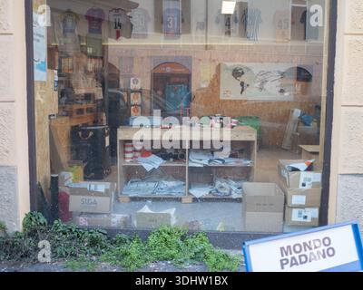 Cremona, Italien 9. Januar 2026 Schaufenster mit einem unorganisierten Arbeitsbereich im Inneren, mit hängenden Sportrikots und Außenreflektionen, mit einem Mo Stockfoto
