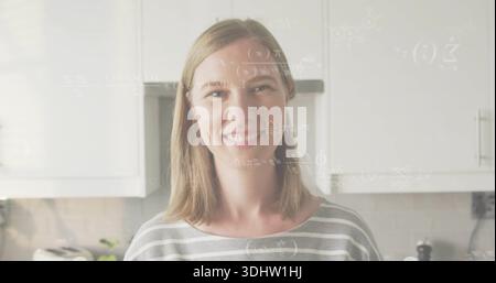 Posierende Frau in grauem gestreiftem Oberteil lächelt in der Küche mit Toaster, Pflanze, Formel-Overlay Stockfoto
