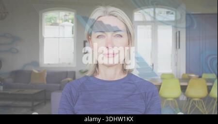 Lächelnde reife Frau mit blauem Sporttop, mit Blick auf die Kamera im Wohnzimmer mit blauen Überzügen Stockfoto