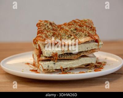 Pistazienschicht-Dessertscheibe aus nächster Nähe mit zerstoßenem Pistazienbelag, Dessertfotografie auf einem Holztisch, Draufsicht. Stockfoto