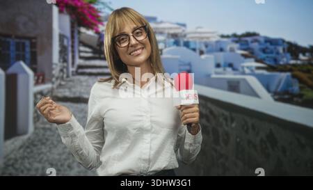 Reporterin mit rotem Mikrofon und Nachrichtenfahne, lächelnd und gestisch mit erhobener Hand, mit Brille und weißem Hemd am Studio-Set; vertrauensvoll Stockfoto