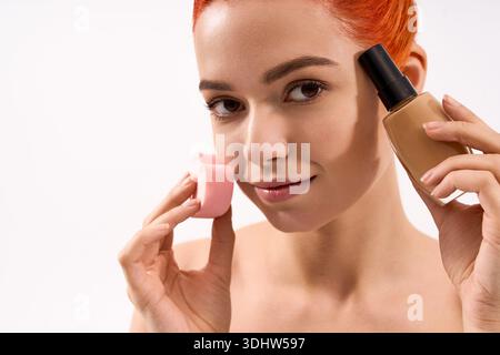 Die schöne Frau zeigt ihre Make-up-Fähigkeiten mit einem Schönheitsmixer und einer Foundation ganz einfach. Stockfoto