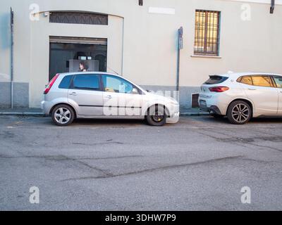 Cremona, Italien 9. Januar 2026 Alte und neue Autos stehen im Kontrast zu einem kompakten silbernen Ford Fiesta auf einem temporären Reserverad, das dicht hinter einem modernen W geparkt ist Stockfoto
