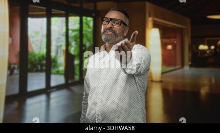 Mann mit Bart und Brille, der die Hand nach vorne streckt und im Gebäude einen Kuss bläst; verspielte Einladung. Stockfoto
